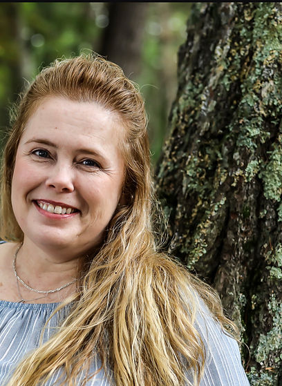 A woman standing next to a tree smiling for the camera.